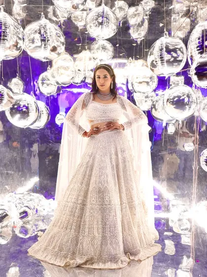 A full view of the showstopper cocktail look. The intricate white lehenga called for makeup that was equally grand. The dramatic, glittering eyes are balanced by luminous skin, creating a look that is pure glamour and sophistication for a night of celebration.