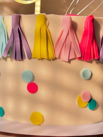 A festive and colorful cake for a first birthday party. This lemon-flavored cake is decorated with a fun tassel garland, confetti dots, and a balloon topper.