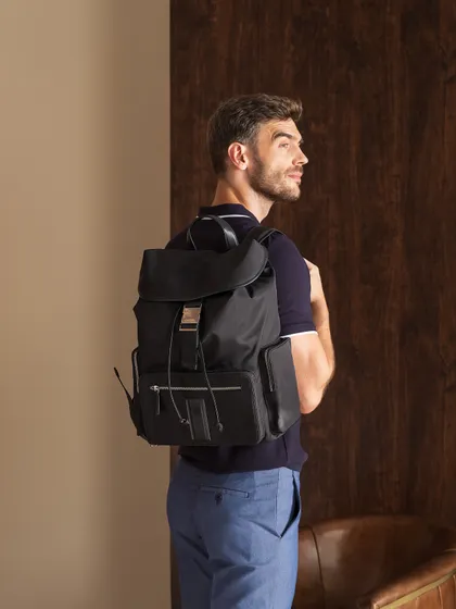 This shot focuses on a backpack from the same men's accessories brand. The styling is casual yet refined, showing how the product can be integrated into an everyday, elevated wardrobe.