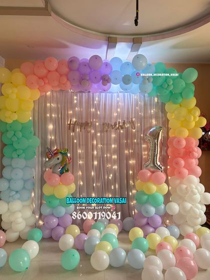 A pastel rainbow unicorn theme for a first birthday. The balloon arch over a curtain with fairy lights creates a dreamy and magical atmosphere.