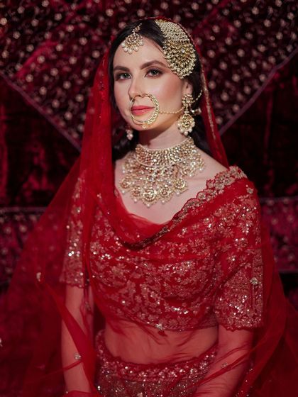 A full portrait of the bride in her red lehenga, showing how a simple, clean hairstyle can be the perfect choice for a heavily embellished outfit.