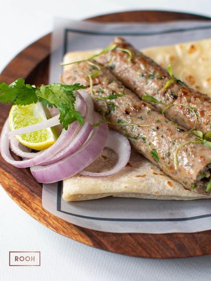 A classic presentation of Gulkand Chicken Seekh, wrapped in a soft Rumali Roti with fresh onions and lime.