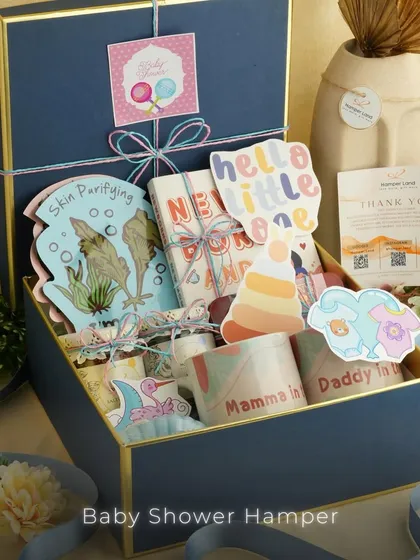 A closer look at a 'Hello Little One' baby shower hamper. This gift box is filled with newborn essentials, cute decorative cutouts, and items for the new parents, like 'Mamma to be' and 'Daddy to be' mugs.