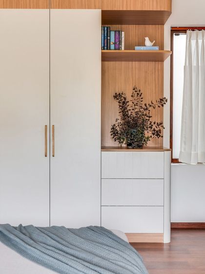 This guest room wardrobe combines white and wood tones, with an open-shelf niche for books and decor, making guests feel right at home.
