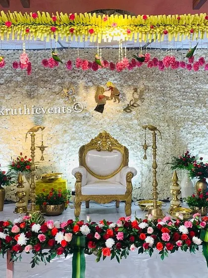 An elegant all-white backdrop made of dense jasmine flowers. The stage is framed by traditional flower pillars and accented with red roses, creating a look of pure sophistication.