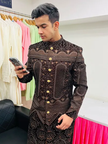 This client is checking his phone while looking sharp in our brown patterned Indo-western three-piece suit.