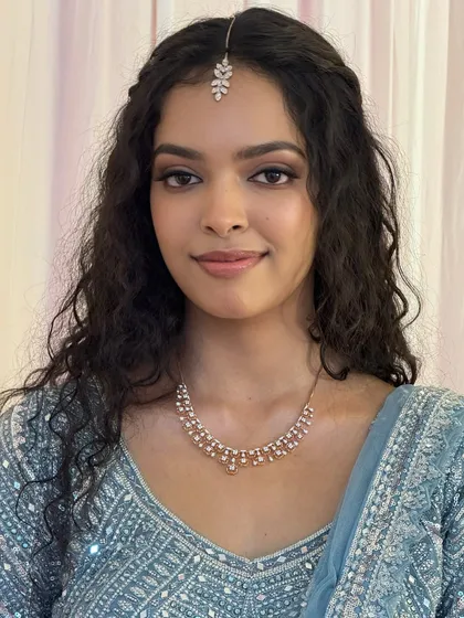 A stunning portrait of Dr. Sushmita for her reception. Her natural curls are styled beautifully, and the makeup is soft and glamorous with a defined eye, perfect for her modern blue lehenga.