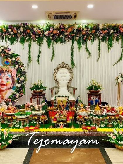 A beautiful baby shower setup with a custom backdrop with a mother and child portrait, surrounded by floral arrangements and a full display of traditional plates.