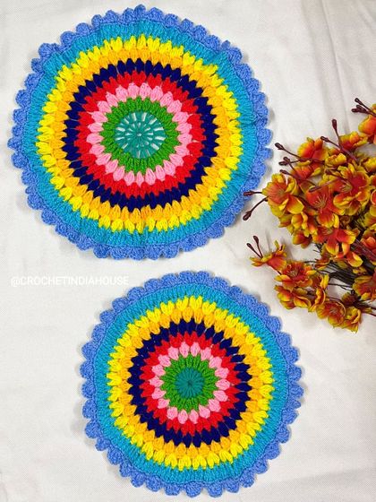 These colorful crochet doilies feature a rainbow-like pattern with a blue scalloped edge, perfect for use as a tablemat or a decorative thali cover.