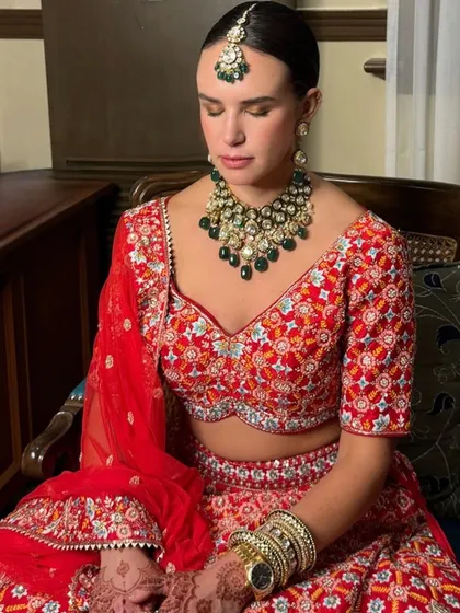 A serene bride captured in a moment of reflection. Her makeup is soft yet defined, with a sleek bun hairstyle that beautifully showcases her emerald green necklace and maang tikka.