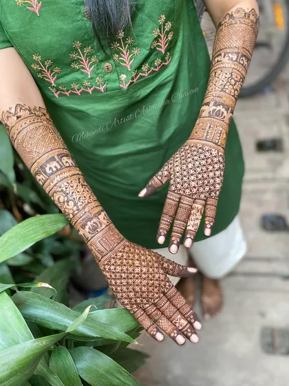 A back-of-the-hand view of a full bridal mehendi. The design features checkerboard patterns and personalized initials, extending all the way up the arms.
