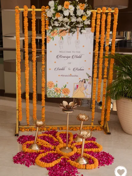 An elegant welcome sign for the "Kesariya Haldi" ceremony, framed by marigold garlands and traditional brass diyas on a bed of rose petals.