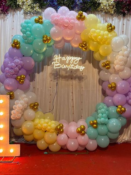 A beautiful pastel rainbow ring for a first birthday celebration. This circular arch uses soft shades of pink, yellow, mint, and lilac, with small gold accents and a neon 'Happy Birthday' sign. The large light-up '1' makes it clear what the special occasion is.