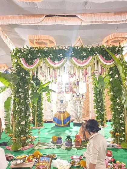 This mandap is designed for a traditional Hindu wedding ceremony, with deities placed at the center. The structure is built with pillars of lush greenery and flowers, with banana trees marking the sacred space.