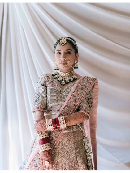 A classic, poised bridal portrait. The bride's intricate lehenga, jewelry, and the clean background come together to create a timeless and elegant image.