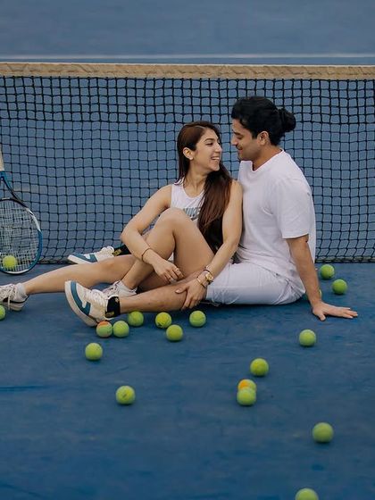 A relaxed moment on the tennis court, surrounded by tennis balls. This shot captures the fun and easygoing chemistry of the couple after a friendly match.