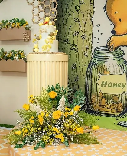 The beautiful cake for the Winnie the Pooh baby shower, placed on a custom stand next to a honey pot prop.