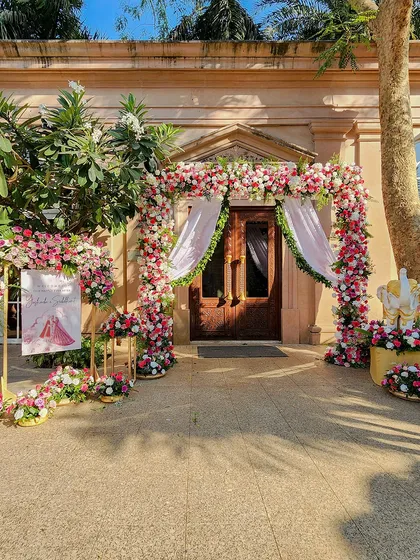 A fairytale entrance for a daytime wedding ceremony. The doorway is framed by a stunning arch of pink and white roses, with matching floral arrangements and a welcome sign to greet the guests.