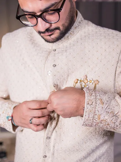 A close-up shot of the groom getting ready, focusing on the details of his embroidered sherwani.