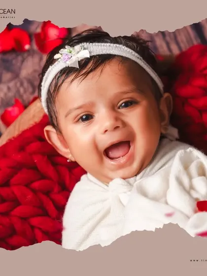 The purest joy in a single frame. This close-up from a newborn session highlights that beautiful, gummy smile, framed by a soft red knit blanket and delicate rose petals for an artistic and tender portrait.