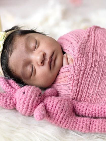 Sleeping soundly in a miniature bed, this newborn is surrounded by soft pink flowers. These styled setups create beautiful, dreamy portraits.