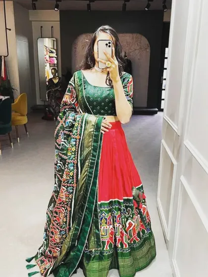 A beautiful art silk lehenga set in a classic red and green combination. The highlight is the intricate Patola and Bandhani print dupatta, which adds a traditional touch. This complete set is perfect for weddings or festive parties.