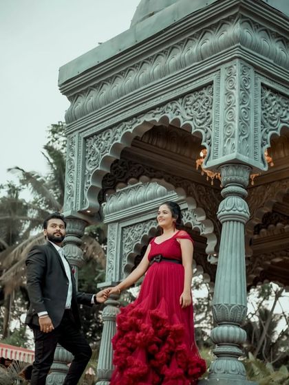 A stylish pre-wedding portrait in front of an ornate structure. The red ruffled gown is a showstopper, perfect for creating a memorable look.