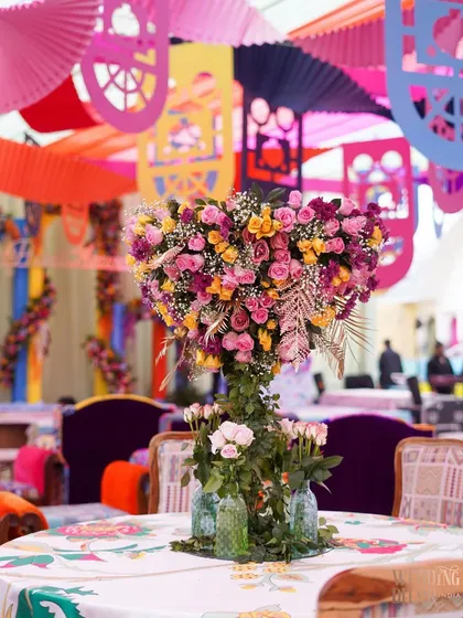 A heart-shaped floral centerpiece for a guest table, made from pink and yellow roses. This romantic detail adds a touch of sweetness to the vibrant and colorful Haldi decor.