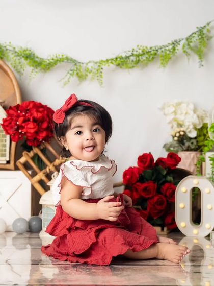 A sweet portrait for a sweet one-year-old. The setup features a romantic theme with red roses, rustic white boxes, and light-up 'ONE' letters.