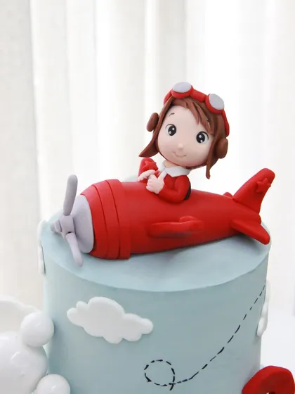 A close-up of the adorable, handcrafted pilot and his red airplane, soaring through the clouds on this special birthday cake.