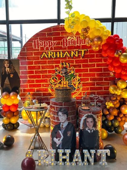 A detailed Harry Potter theme decoration, featuring a brick wall backdrop with the Hogwarts crest, character cutouts, and balloons in house colors.