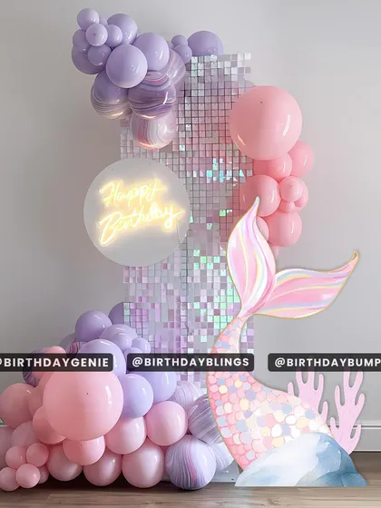 A chic and modern mermaid theme with a pastel purple and pink shimmer wall. A neon "Happy Birthday" sign and a large, iridescent mermaid tail cutout make this a stylish and eye-catching design.