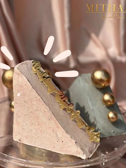This is a slice of edible sculpture. The cake is cut into a unique geometric shape and frosted with natural colors, then decorated with a custom "Birthday" topper and shimmering gold spheres.