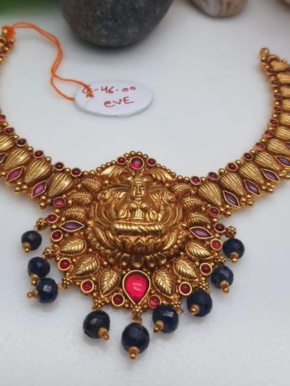 A unique temple necklace with a leaf-like design along the chain. The central goddess pendant is surrounded by colorful stones and dark blue bead drops.