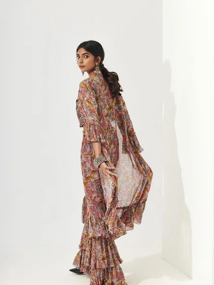 A back shot showing the beautiful flare of a ruffled sharara. The makeup, visible from the side, is clean with a neatly tied-back hairstyle, creating a polished and sophisticated profile.