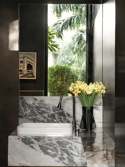 Even small spaces like a powder room can tell a story. Here, a custom marble vanity with a waterfall edge is set against a large mirror that reflects the lush greenery outside, making the room feel connected to nature.