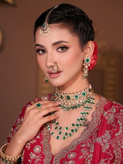 A detailed shot of this royal bridal look, focusing on the harmony between the makeup and the stunning emerald jewelry. The eyes are softly defined and the skin is luminous, creating a truly regal presence.