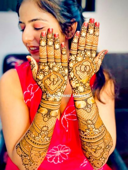 A happy bride-to-be with her engagement mehndi. The design includes her initials 'R' and 'K' inside a floral motif, a beautiful way to celebrate her union.