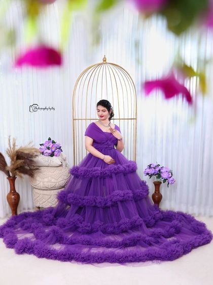A vision in purple. This studio portrait features a mother-to-be in a voluminous ruffled gown, seated elegantly in a golden birdcage chair.