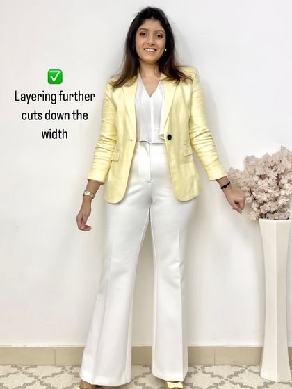 This image shows how adding a third layer, like this yellow blazer, over a monochrome white outfit further cuts down perceived width and creates a chic, polished look.