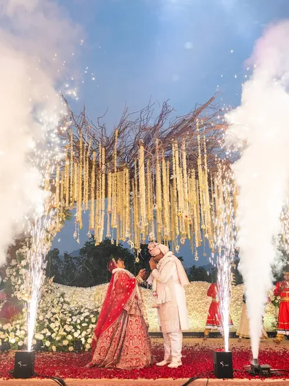 The couple exchanges garlands under a shower of smoke and fireworks, creating a dreamy, ethereal atmosphere for their union.