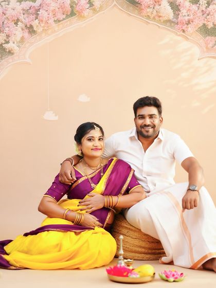 A classic portrait of a couple during their traditional maternity shoot. They are seated together in a studio setup designed for a timeless, cultural feel.