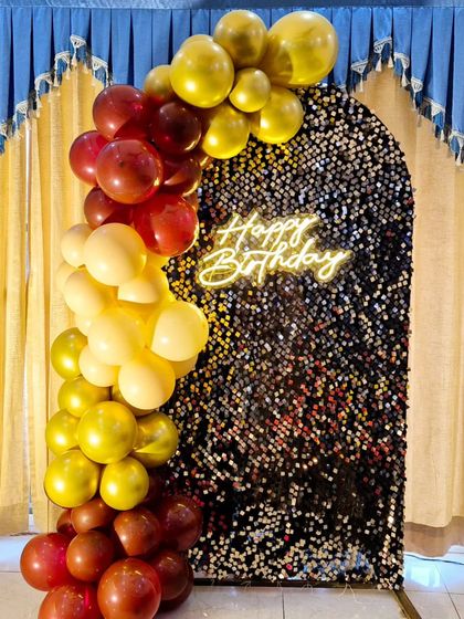 A rich color combination of maroon and gold balloons framing a black shimmer arch with a 'Happy Birthday' neon sign.