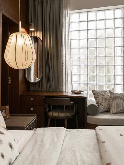 The bedroom vanity and desk area, lit by a stylish pendant lamp. The dark wood paneling and oval mirror create a sophisticated and personal corner within the larger room.