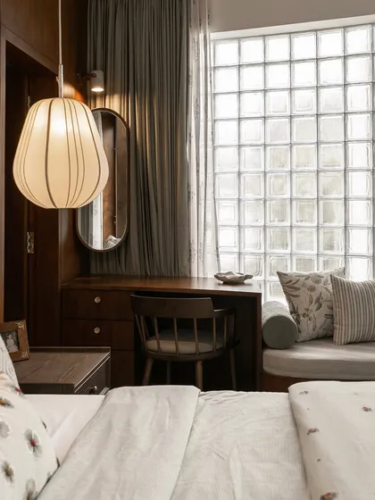 The bedroom vanity and desk area, lit by a stylish pendant lamp. The dark wood paneling and oval mirror create a sophisticated and personal corner within the larger room.