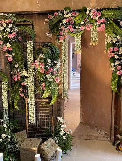 A modern take on entrance decor. We used a unique combination of woven green leaves, pink roses, and hanging floral strings against a metal grid for a contemporary and artistic look.