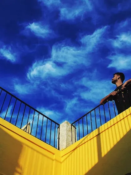 Looking up from a yellow balcony at a dramatic, deep blue sky. The strong lines and vibrant colors create a feeling of sunshine on a cloudy day, a moment of pure visual joy.