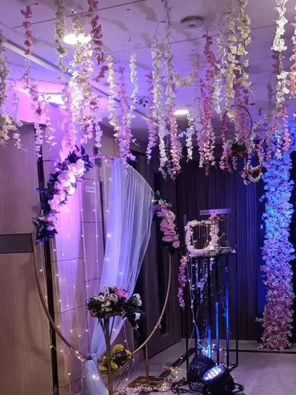 A dreamy and whimsical engagement or reception backdrop. This setup features a ceiling of hanging pink and white wisteria, a circular arch with fairy lights, and dramatic uplighting to create an enchanting atmosphere.