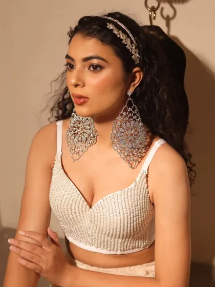 A closer view of the makeup for a fashion accessory shoot. The skin is flawless and radiant, with a soft contour and a neutral lip, allowing the statement earrings and headband to be the main focus.