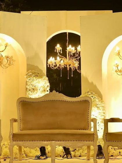 Another view of the elegant white reception stage, showing the vintage-style furniture and the warm glow of the chandeliers.